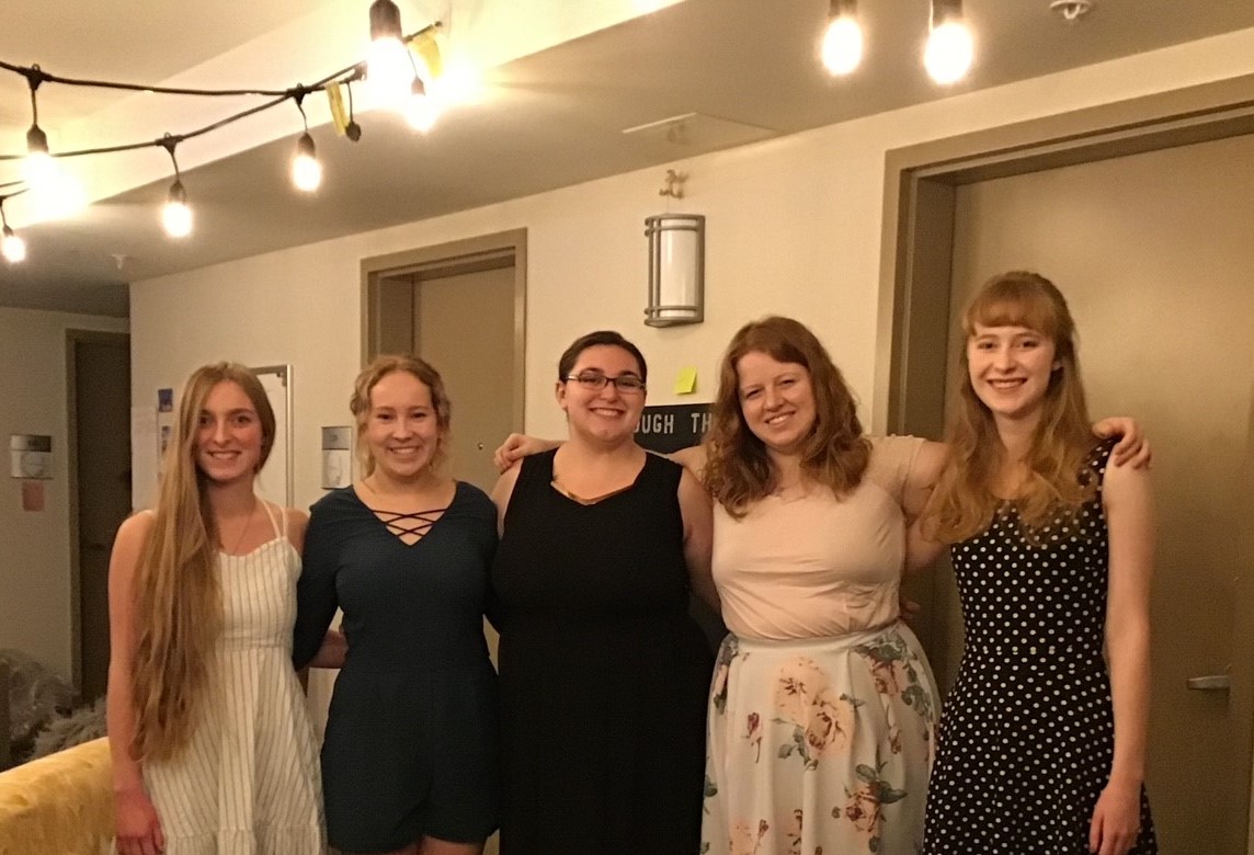 five young women standing in a hallway beneath lights