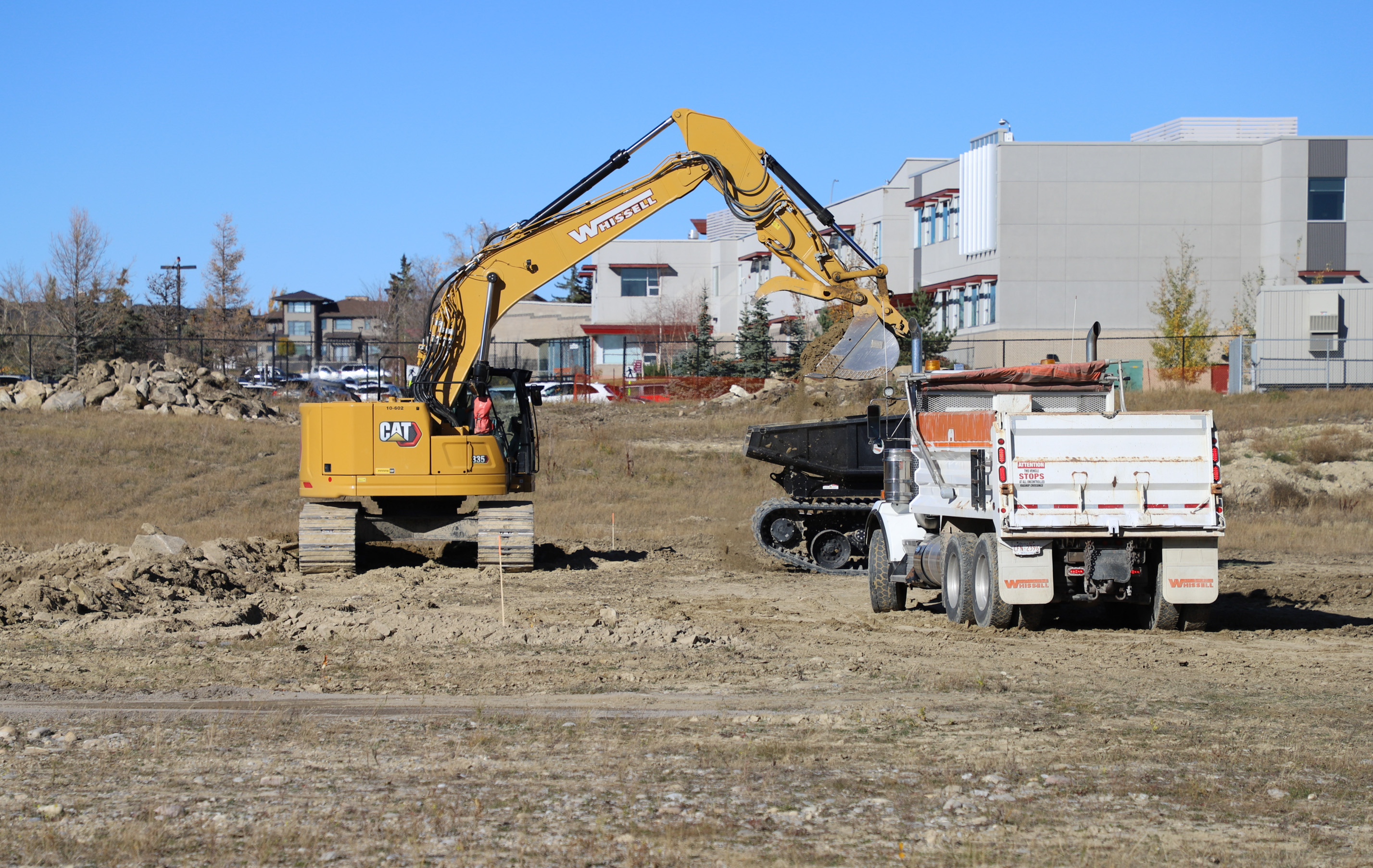 Backhoe emptying dirt into waiting dump trucks